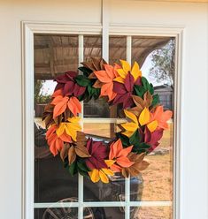 a wreath on the front door of a house with autumn leaves hanging from it's side