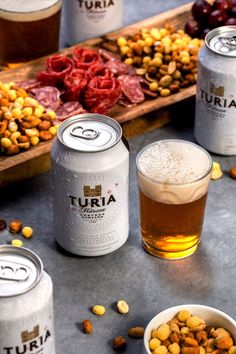 beer cans and bowls filled with nuts next to some drinks on a table that has food in them