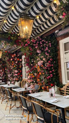 an outdoor dining area with striped awnings and flowers on the wall behind it