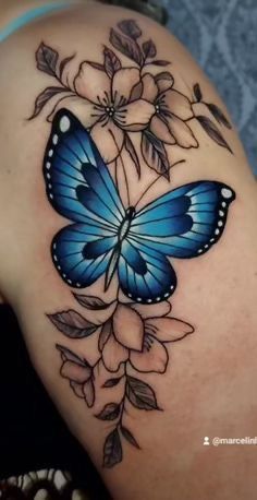 a blue butterfly on the back of a woman's shoulder with flowers around it