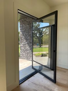 an open glass door in a room with wood flooring and stone wall behind it