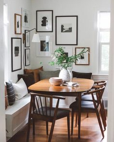 a dining room table with chairs and pictures on the wall above it in front of a couch