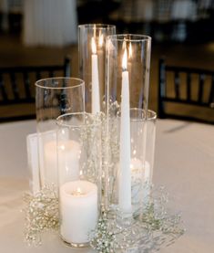 candles and flowers on a table in a room with white linens, chairs and tables