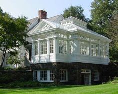 a large white house sitting in the middle of a lush green field next to trees