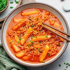 a bowl filled with noodles and carrots on top of a white table next to chopsticks