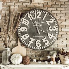 a large clock on the side of a brick wall above a mantle with pumpkins and gourds