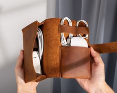 a hand holding a brown leather case with multiple cords in it and an apple charger attached to the inside