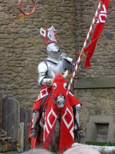 a man in armor riding on the back of a horse holding a red and white flag