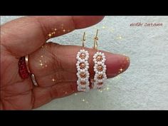 a hand holding two pairs of white and brown beaded hoop earrings on top of each other