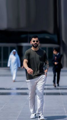 a man in black shirt and white pants walking down street with other people behind him