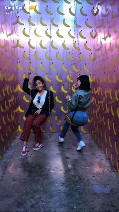 two girls are posing in front of a wall with bananas hanging from it's sides