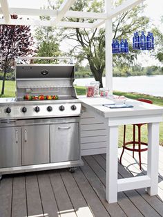 an outdoor kitchen with stainless steel appliances and bar stools on the back deck area