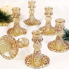 a group of glass candlesticks sitting on top of a table next to a pine tree