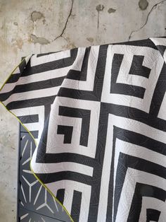 a black and white quilt with yellow trim on a chair in front of a concrete wall