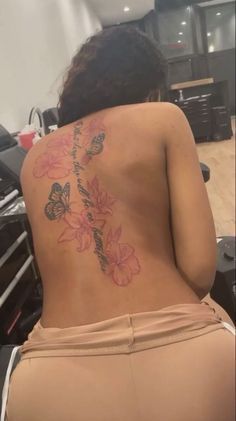 the back of a woman's body with flowers on it and butterflies tattooed on her lower back