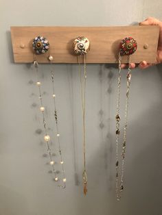 a person holding up a wooden rack with jewelry hanging from it's sides on the wall