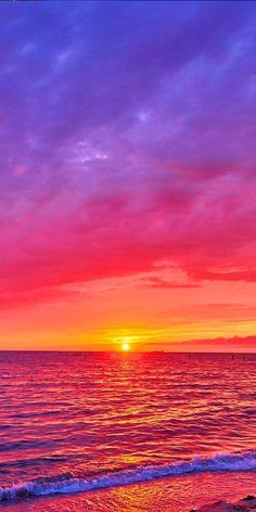 the sun is setting over the ocean with pink and purple clouds in the sky above it