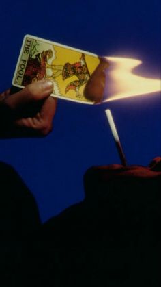 a person holding a lit match card in their hand with a blue sky behind them