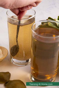 a person holding a spoon over a glass filled with tea and other items on a table