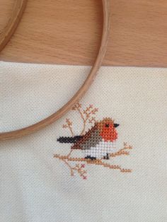 a cross stitched bird sitting on top of a white cloth next to a wooden handle