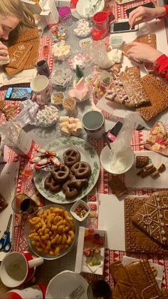 people sitting at a table covered in cookies and pretzels, with plates of food on the table