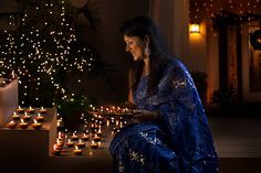 a woman sitting in front of a christmas tree holding a tray with lit candles on it