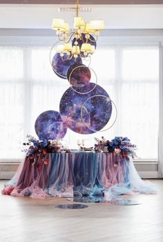 the table is covered with purple, blue and red cloths as it sits in front of a large chandelier