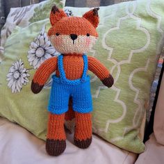 an orange knitted fox doll sitting on top of a bed next to a pillow