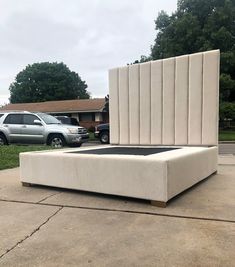 a large bed sitting on top of a cement slab in front of a car park