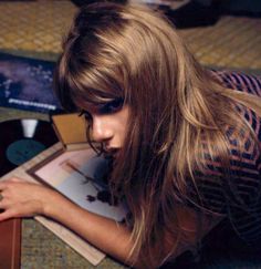 a woman with long hair sitting on the floor next to a record player and looking down at it