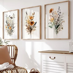 three framed flowers are hanging on the wall above a wicker chair and side table