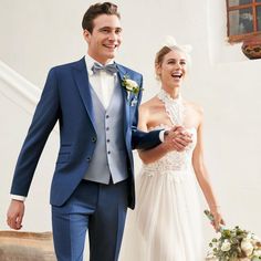 a bride and groom are walking down the stairs at their wedding day, dressed in blue tuxedos