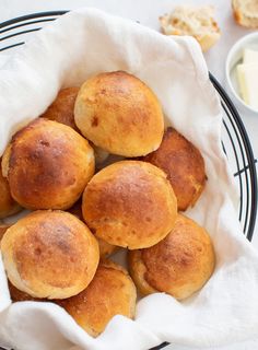 several rolls in a basket on a table with butter and other food items around it