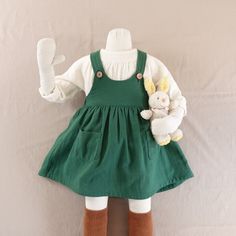 a doll dressed in green and white holding a stuffed animal with brown socks on it's feet