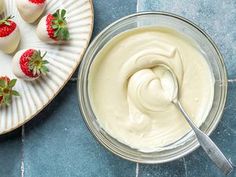 some strawberries and cream in a bowl on a blue table with a white plate