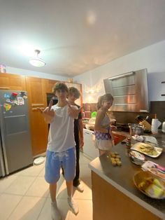 two children are standing in the kitchen and one is pointing at something on the counter