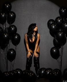 a woman sitting in front of black balloons with her legs on the ground and one hand on her hips