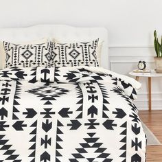 a bed with black and white bedspread on it in a room next to a plant