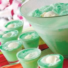 green jello with whipped cream in a bowl and six glasses lined up on a table