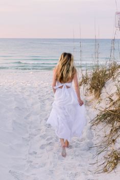 a woman in a white dress walking on the beach