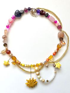 This gorgeous necklace has a variety of mixed glass, seed, and unique beads to create an ombre effect reminiscent of the sunset. It also holds three handmade and handpainted glazed clay charms (the sun and stars) that glimmer in the light due to their gold detailing. It is ~18 in. long with extra chains to customize to a length that fits you best.  To ensure long-lasting wear of this necklace, keep away from water, perfume, and chemicals. It is also recommended not to wear while sleeping, playing sports, or showering. The clay pieces can be broken so handle with care :) Yellow Glass Beaded Necklace, Handmade Rainbow Glass Necklaces, Adjustable Whimsical Beaded Necklaces, Whimsical Adjustable Beaded Chain Necklaces, Bohemian Yellow Glass Necklace, Whimsical Adjustable Beaded Chain Necklace, Festival Fairycore Beaded Jewelry, Fairycore Beaded Festival Jewelry, Fairycore Beaded Jewelry For Festivals