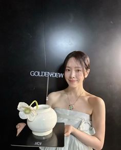 a woman in a white dress is holding a vase with a flower on it and posing for the camera