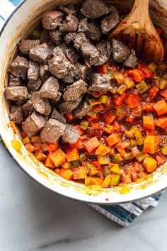 cooked meat and vegetables in a pot with a wooden spoon next to it on a towel