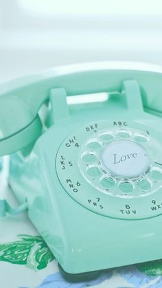 an old fashioned green phone sitting on top of a floral table cloth with the word love written on it