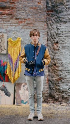 a man standing in front of a brick wall with paintings on the walls behind him