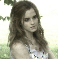 a young woman with long hair standing in front of some trees and grass, looking at the camera