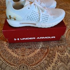 a pair of white under armour shoes sitting on top of a red box with gold lettering