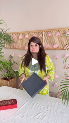 a woman sitting at a table with a laptop in front of her and pink flowers behind her