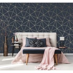 a bed with pillows and blankets on it in front of a wall that has geometric designs