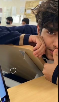 a young man sitting at a desk with a laptop computer in front of his face